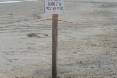 A sign on a wooden post reads 'NO LIFEGUARDS BEYOND THIS POINT' on a deserted, sandy beach.