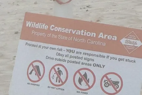 Sign for 'Wildlife Conservation Area' with rules and a life preserver on a sandy background.