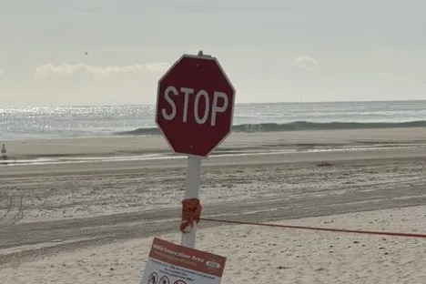 Tilted stop sign on sandy beach with cloudy sky.