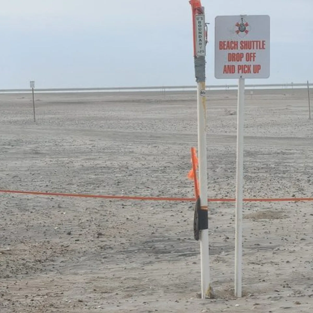 Beach shuttle drop-off sign on a sandy shoreline.
